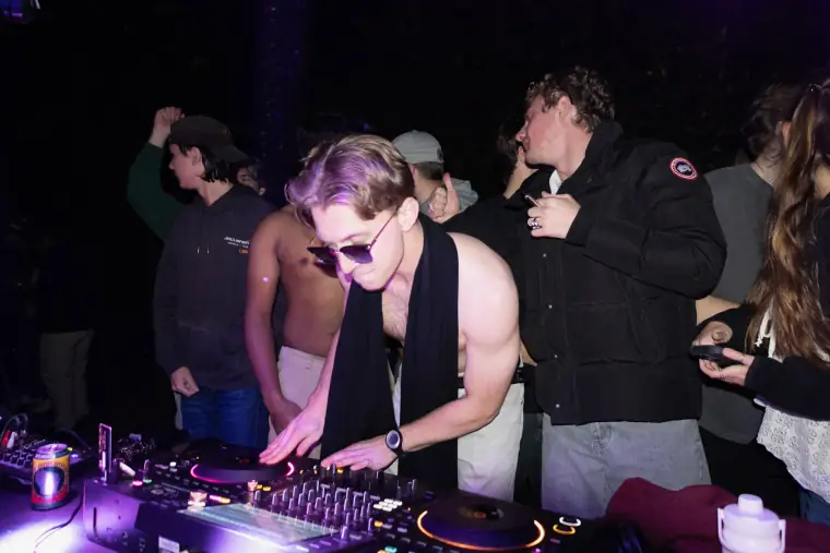 DJ mixing in purple light with people gathered around